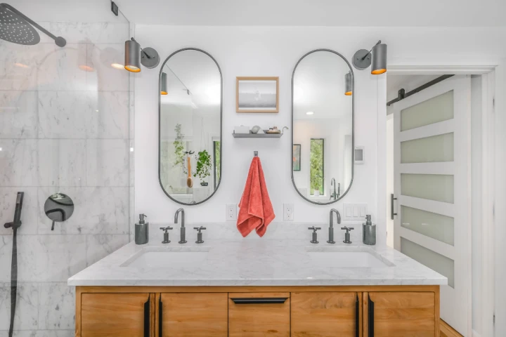 wooden vanity unit with a large white ceramic sink and two oval mirrors with black frames