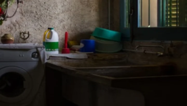 A dirty sink and a bucket and a bottle of detergent.