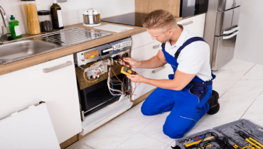 A person in blue overalls working on a kitchen.